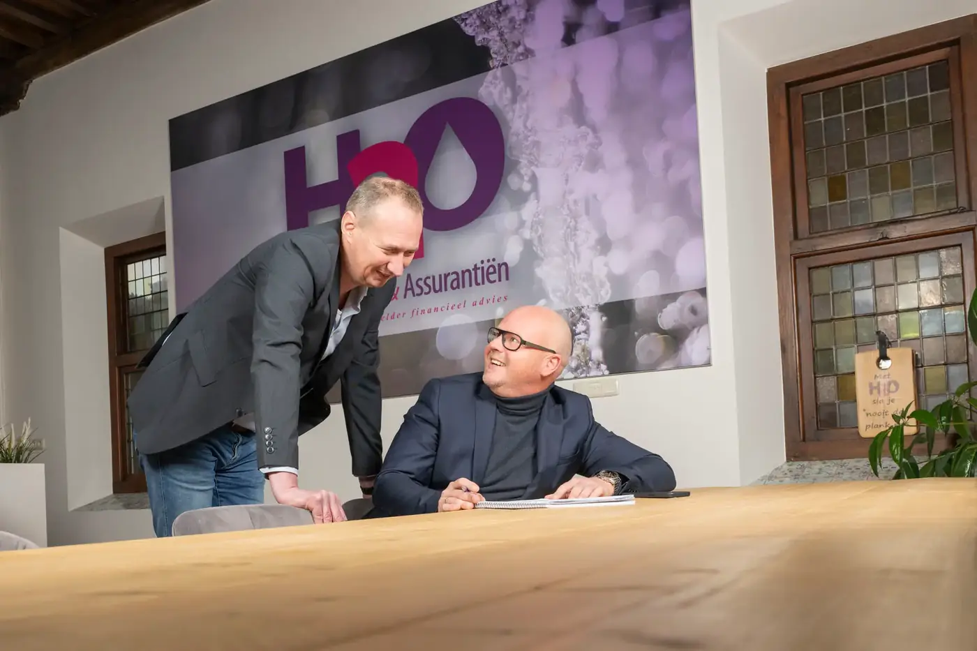 Patrick en Erwin aan tafel op het kantoor van H2O, met het logo op de wand